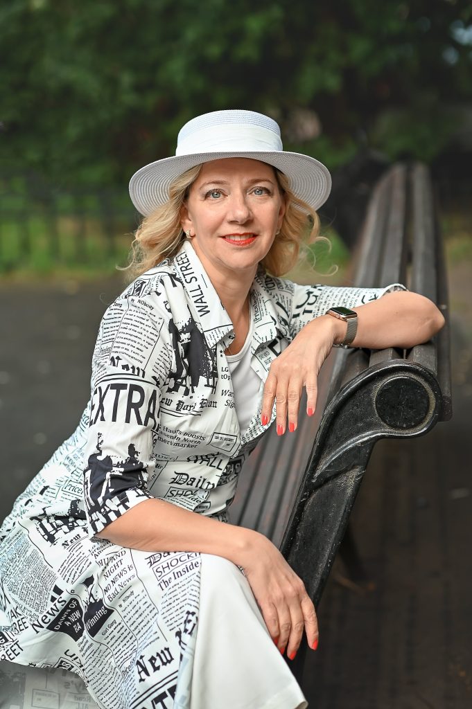 Anna Rikko seated on a park bench wearing a white hat